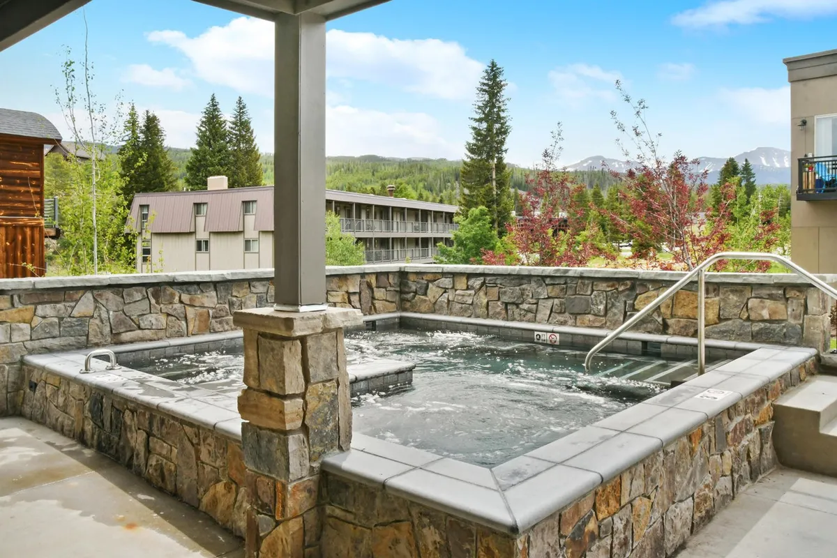 A tranquil exterior shot showcasing a large, communal hot tub nestled in a scenic setting, with a breathtaking mountain backdrop. The image suggests a relaxing, social environment suitable for unwinding after adventurous days.