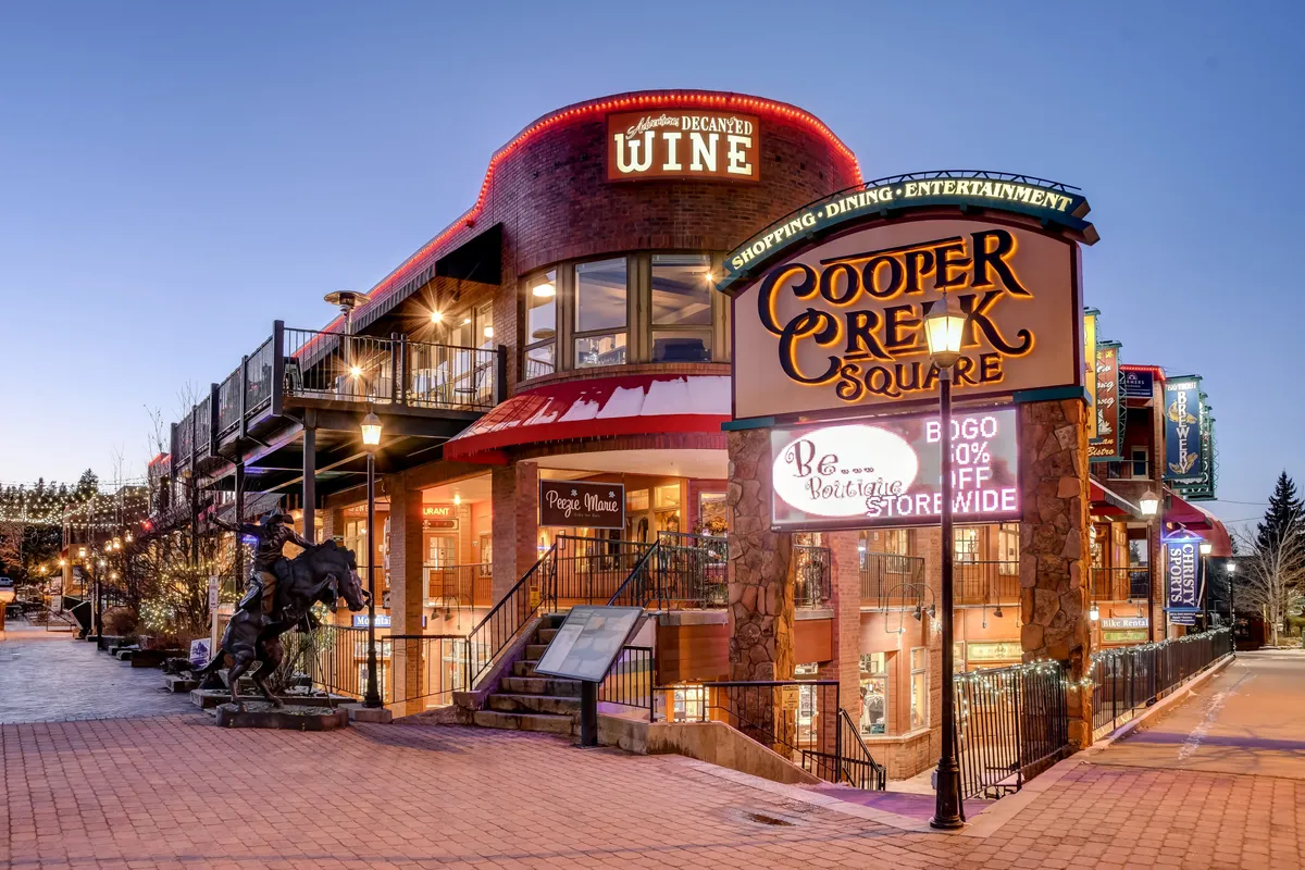 This image showcases the Cooper Creek Square sign along with a wine shop sign and decorative lighting. The scene is festive, suggesting an area bustling with shopping, dining, and entertainment options. The mood is vibrant and inviting, hinting at live music performances, seasonal markets, and unique local experiences.