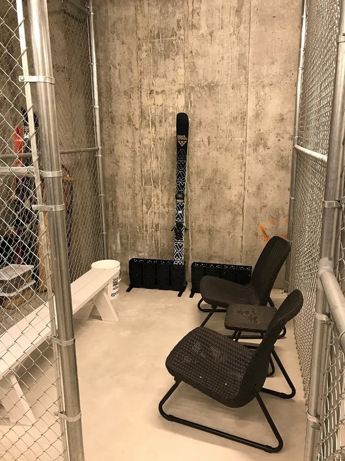 An interior image capturing a practical gear storage space with ski equipment and a seating area, set against concrete walls. The space feels functional and ready for skiers and boarders to transition easily from adventure to relaxation.